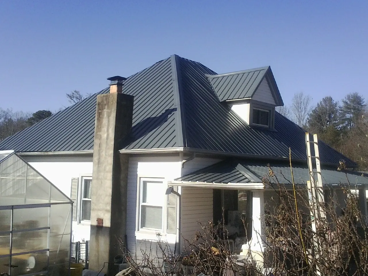 Dark blue standing seam metal roof on a white farmhouse with dormer — Slate & Tile Roof Repair by Roofing Brothers in Steens