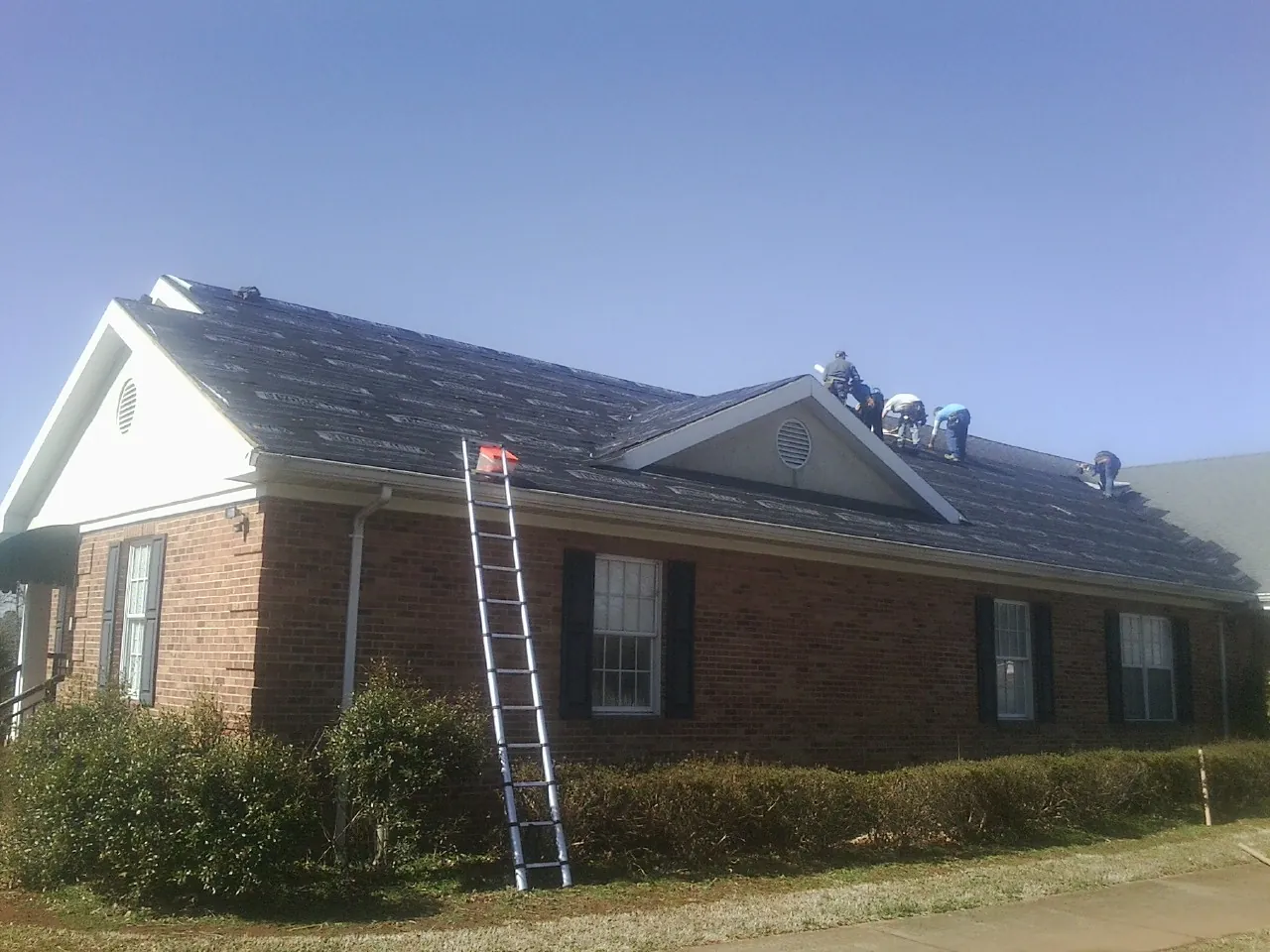 Crew tearing shingles off a brick ranch roof with a ladder set — Metal Roof Repair work by our crew in Steens