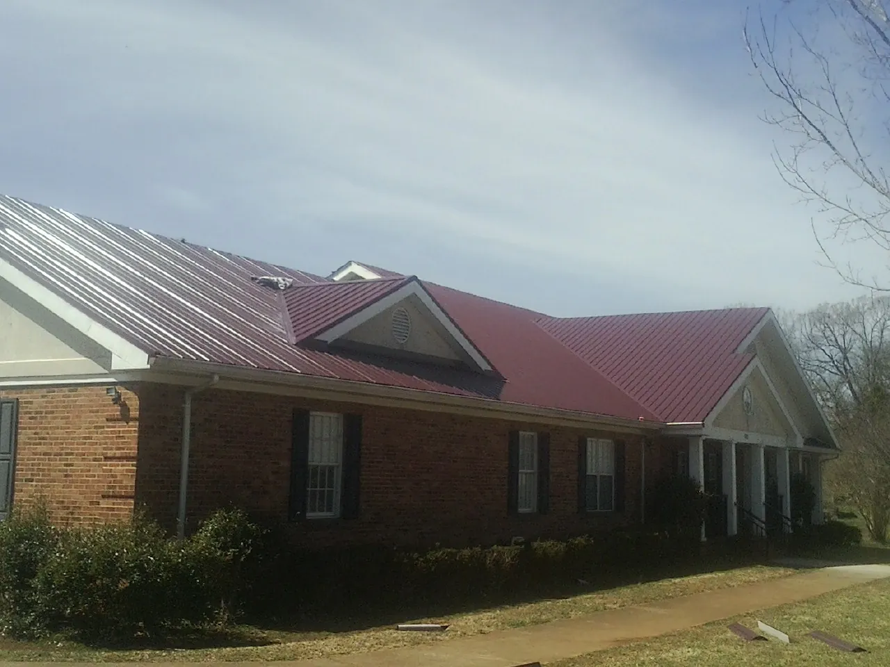 Red metal roof with gabled entries on a long brick building, from a Hail Damage Roof Repair job in Steens