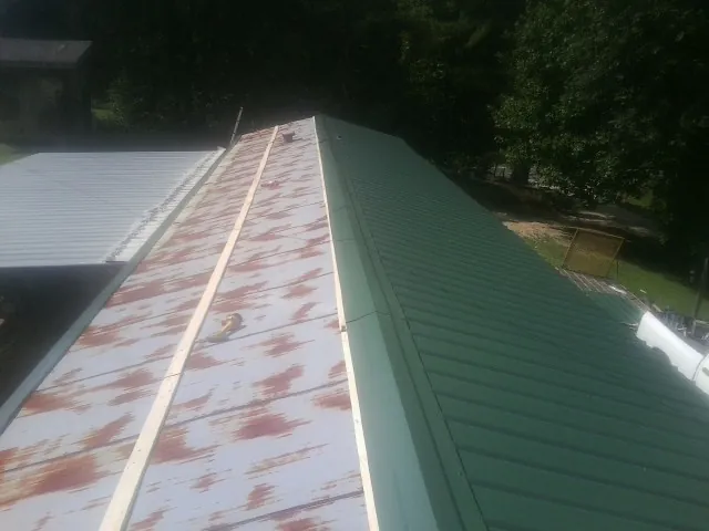 Old rusted panels beside newly installed green metal roofing — Wind Damage Roof Repair by Roofing Brothers in Steens