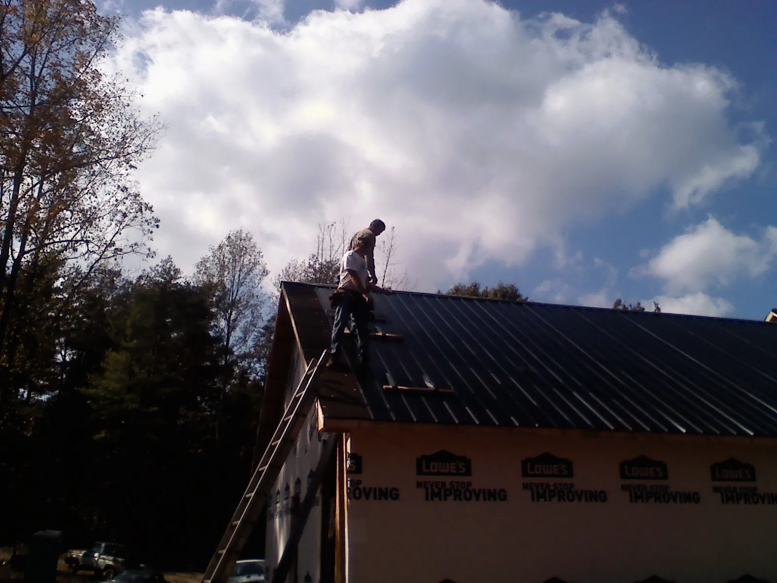 Roofer fastening dark metal panels high against a cloudy sky, from a Roof Inspection job in Steens