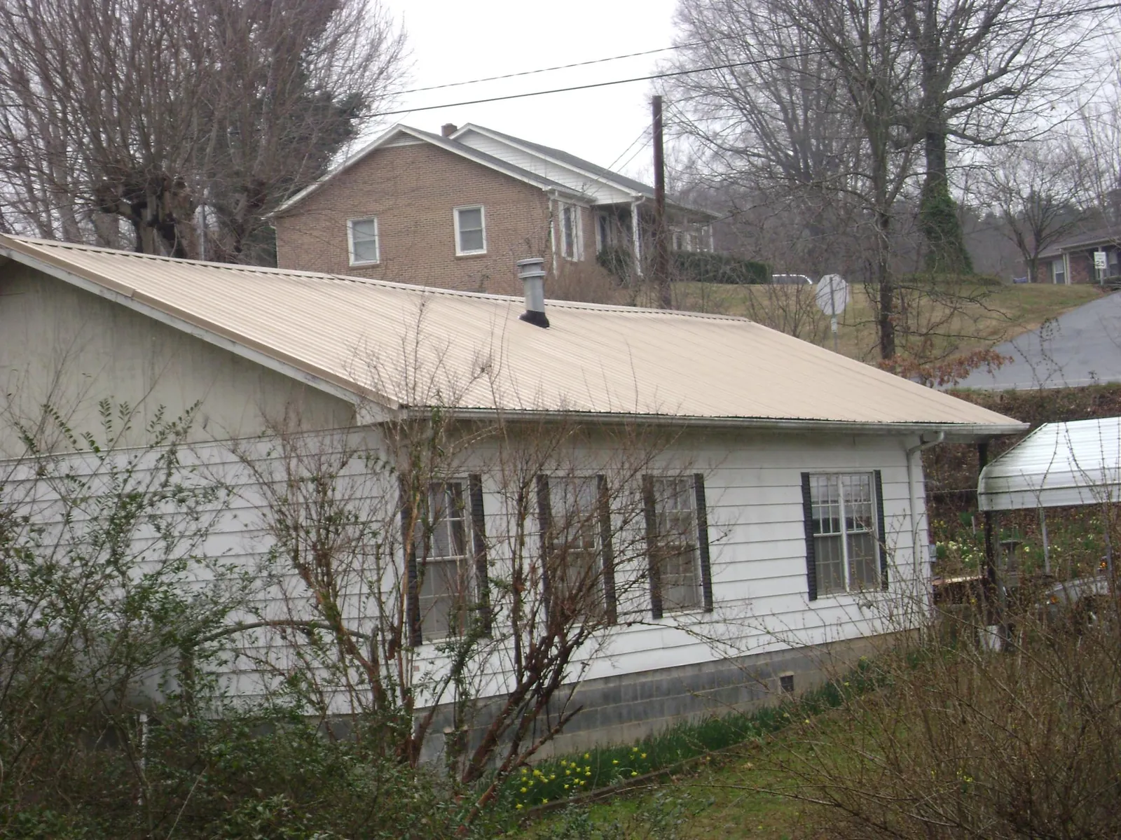 Tan metal roof on a white sided house set into a hillside — Commercial Roofing by Roofing Brothers in Steens