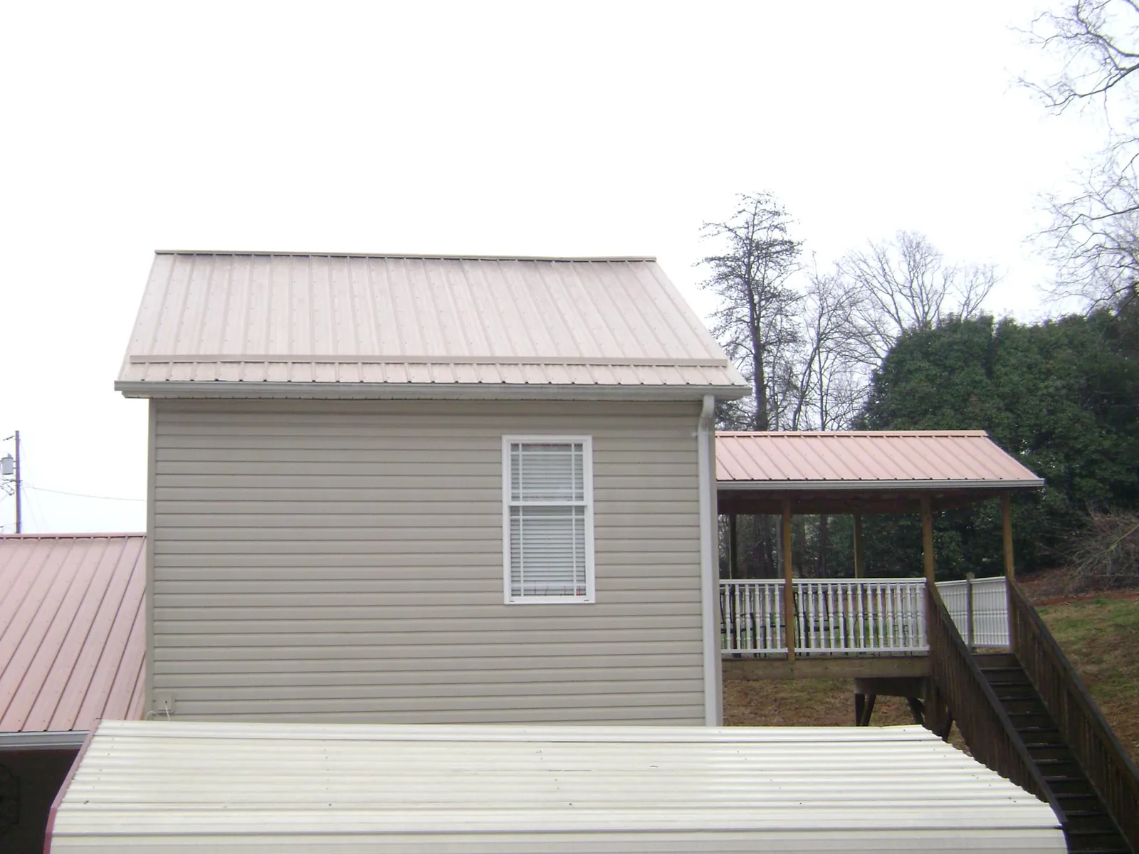 Tan metal roofs on a two story addition and attached porch, from a Roof Replacement job in Steens